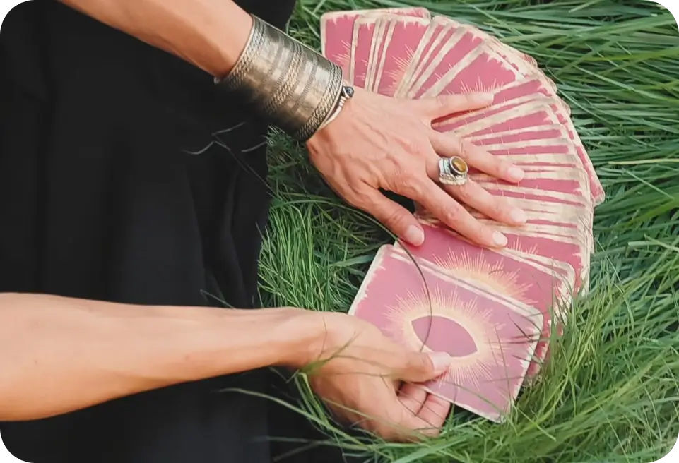 Manos desplegando en abanico las cartas de oráculo sobre la hierba
